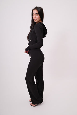 The model is wearing a black noir Malibu Zip Up Hoodie and Women's Cord Pants by Chloe Colette.