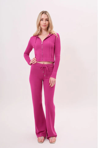 The model is wearing a raspberry taffy Malibu Zip Up women's hoodie and cord pants by Chloe Colette.