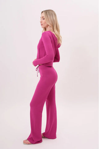 The model is wearing a raspberry taffy Malibu Zip Up women's hoodie and cord pants by Chloe Colette.