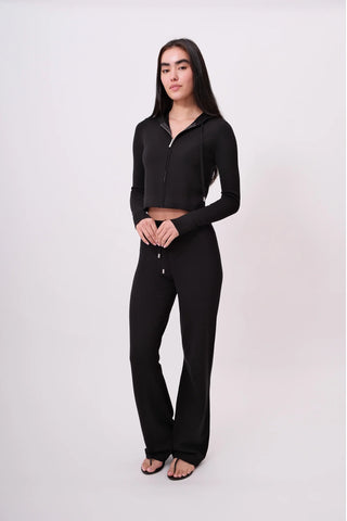 The model is wearing a black noir Malibu Zip Up Hoodie and Women's Cord Pants by Chloe Colette.