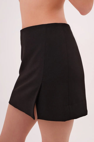 Model wearing a black Jenny Satin Slit Mini Skirt by Chloe Colette showing the side view.