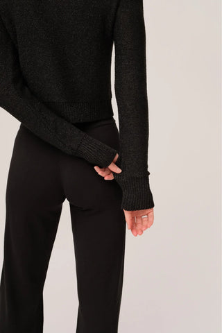 The model is wearing a black quartz Jolie Lite-knit sweater by Chloe Colete with black jogging pants showing the back side view.