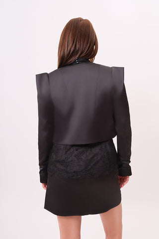 The model is wearing a juliette satin jacket in black tourmaline and Jenny Mini Skirt by Chloe Colette showing the back side view.