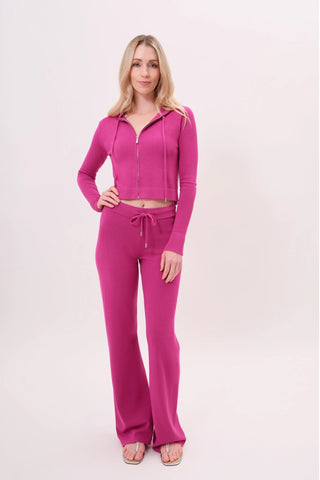 The model is wearing a raspberry taffy Malibu Zip Up hoodie and cord pants by Chloe Colette.