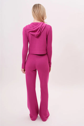 The model is wearing a raspberry taffy Malibu Zip-Up women's hoodie and cord pants by Chloe Colette.