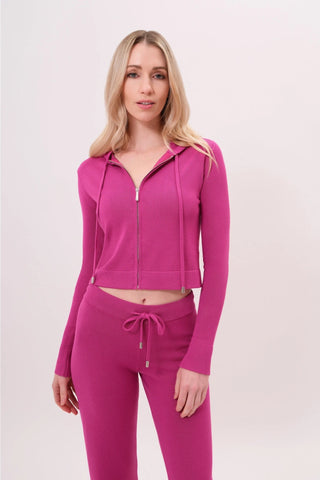 The model is wearing a raspberry taffy Malibu Zip Up hoodie and cord pants by Chloe Colette.