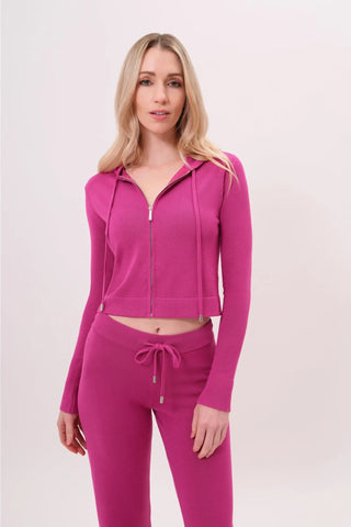The model is wearing a raspberry taffy Malibu Zip Up women's hoodie and cord pants by Chloe Colette.