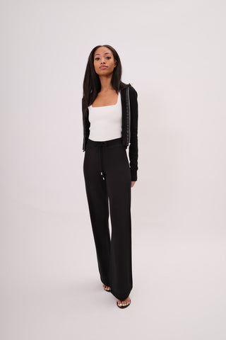The model is wearing a black noir Malibu Zip Up women's Hoodie and Cord Pants by Chloe Colette.