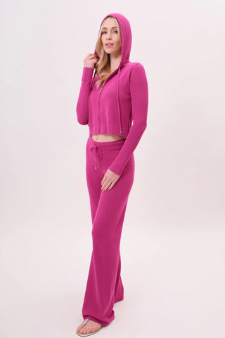 The model is wearing a raspberry taffy Malibu Zip Up women's hoodie and cord pants by Chloe Colette.