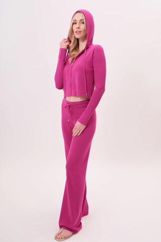 The model is wearing a raspberry taffy Malibu Zip Up hoodie and women's cord pants by Chloe Colette.